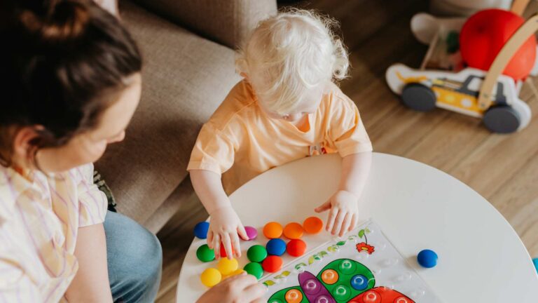 Adult and toddler playing with colorful toys at a small table, showing early signs of autism in toddlers