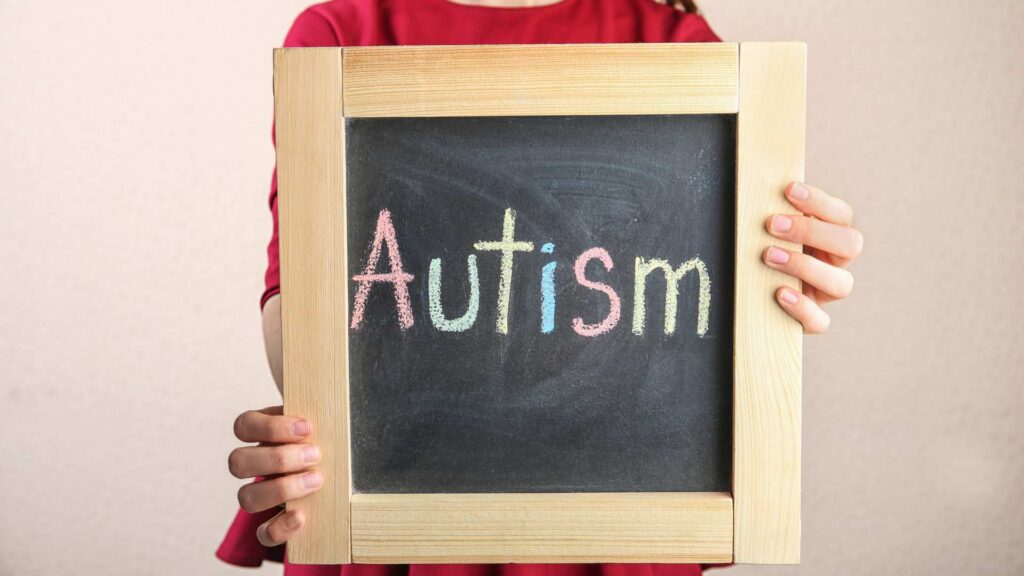 Chalkboard with Autism written in soft pastel colors held by a child